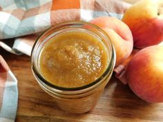 a glass jar filled with peanut butter next to peaches on a wooden cutting board