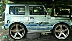 an old blue car parked under a covered area with trees in the backgroud