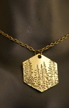 Immerse yourself in the tranquility of nature with this beautifully crafted Gold Pine Tree Necklace. Featuring an intricately etched forest scene on a hexagonal gold-tone pendant, this timeless accessory celebrates the beauty and resilience of pine trees. Whether you're a nature lover, hiker, or simply drawn to the peacefulness of the woods, this necklace is a meaningful addition to your collection. ✨ Symbolism of the Design: - Pine Trees: Represent endurance, peace, and eternal life, serving as Nature-inspired Brass Necklace For Gift, Tree Necklace, Pine Trees, Pine Tree, Lake City, Salt Lake City, A Necklace, The Forest, Timeless Beauty