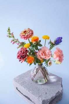 a vase filled with colorful flowers sitting on top of a cement block in front of a blue wall