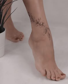 a woman's bare foot with a flower tattoo on her left leg and plant in the background