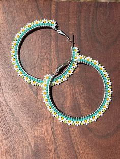 two pairs of beaded hoop earrings sitting on top of a wooden table