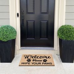 a welcome mat is placed in front of a door with two potted plants on it