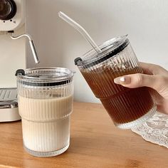 a person is holding a glass with some liquid in it and an espresso machine behind them