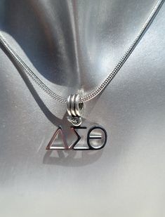 a silver necklace with the letter k and an e on it's side, sitting on a shiny surface