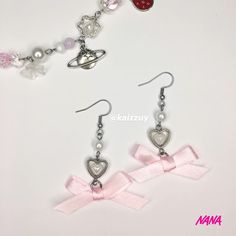 two pairs of earrings with pink ribbon and charms attached to them, sitting on a white surface