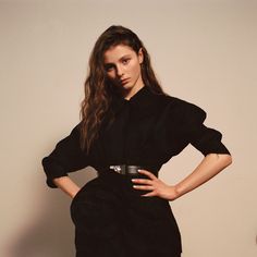 a woman is standing with her hands on her hips wearing a black dress and belt