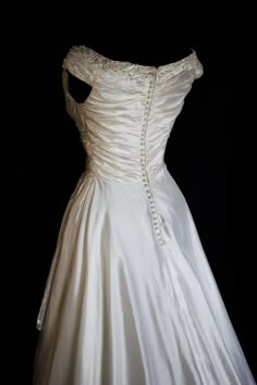 a white wedding dress with beading on the shoulders and neckline, in front of a black background