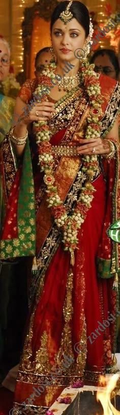 a woman in a red and gold wedding dress with her hands on her chest, standing next to other people