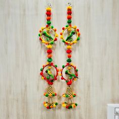 two pairs of colorful beaded earrings hanging from hooks on a wall next to a light switch