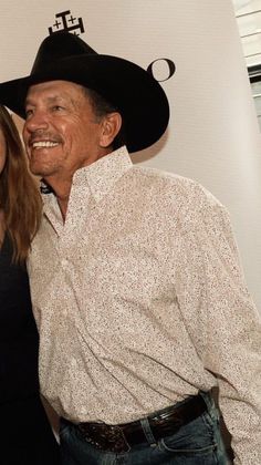 two people standing next to each other in front of a white wall wearing cowboy hats