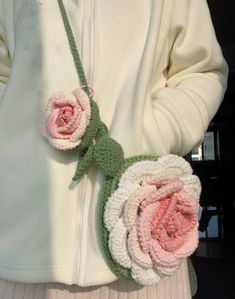 a woman wearing a white jacket with pink flowers attached to her waist and holding onto a green crocheted flower