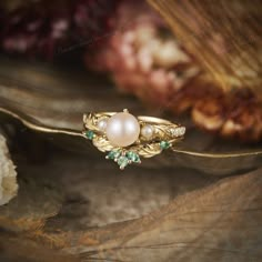 a gold ring with pearls and emeralds sitting on top of a piece of wood