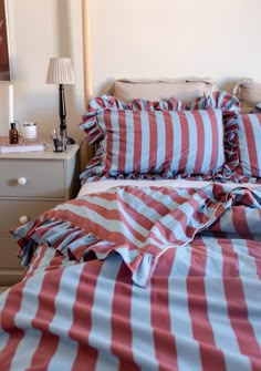 a bed with red and white striped comforter on it's side next to a night stand