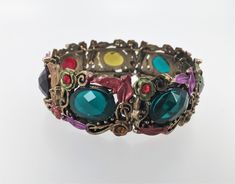 "Vintage bracelet bangle with different colors of fake stones- red, blue, brown, purple and olive green  Approx. Inner Diameter - 2 3/8\", adjustable Approx. Width- 3/4'' Length:  ~8'' Lead & Nickel Safe" Vintage Multicolor Jeweled Bracelets, Adjustable Jeweled Bangle Bracelets, Adjustable Crystal Costume Jewelry Bracelet, Multicolor Costume Jewelry Bangle, Adjustable Jeweled Metal Cuff Bracelet, Costume Jewelry Metal Bangle Crystal Bracelet, Costume Crystal Bangle Bracelet In Metal, Multicolor Costume Jewelry Bracelets With Jewels, Multicolor Jewel Costume Jewelry Bracelets