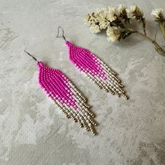 two pairs of pink and white beaded earrings next to some flowers on a table