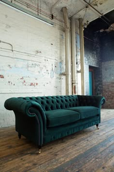 a green couch sitting on top of a wooden floor next to a white brick wall