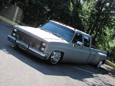 a silver truck parked on the side of a road next to some trees and bushes