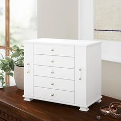 a white dresser sitting on top of a wooden table next to a potted plant