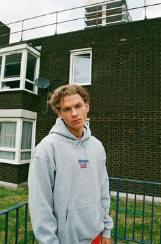 a man standing in front of a brick building Sporty Spring Sweatshirt With Logo Detail, Sporty Spring Sweatshirt With Logo, Streetwear Hoodie With Logo And Relaxed Fit, Logo Detailed Relaxed Fit Hoodie For Streetwear, Relaxed Fit Streetwear Hoodie With Logo, Relaxed Fit Hoodie With Logo For Streetwear, Casual College Sweatshirt With Logo Detail, Casual College Sweatshirt With Logo, Relaxed Fit Hoodie With Embroidered Logo For Streetwear