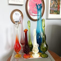 colorful glass vases sitting on top of a table in front of pictures and paintings