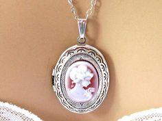 "Romantic Victorian cameo locket necklace with a pendant of a neoclassical woman and flowers against a burgundy red cameo background. The cameo is set in a light weight oval silver plated locket decorated with outer etchings, and you have your choice of a shiny silver finish (shown), gunmetal, and antiqued silver. Also available in gold or bronze. The open locket can hold 2 pictures, and hangs on a rhodium (white gold) plated chain. Length: 18 inches, Locket Pendant: 1.5 inches Please leave a no Charming Silver Necklace For Wedding, Elegant Cameo Necklaces For Wedding, Elegant Cameo Necklace For Wedding, Elegant Cameo Locket Necklace For Wedding, Vintage Cameo Locket Necklace For Wedding, Elegant Vintage Charm Locket Necklace For Formal Occasions, Elegant Formal Locket Necklace With Vintage Charm, Elegant Locket Necklace With Vintage Charm For Formal Occasions, Formal Round Pendant Locket Necklace