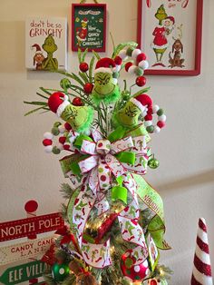 a christmas tree decorated with green, red and white ornaments in front of pictures on the wall