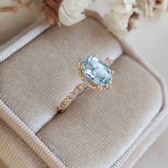 an engagement ring with a blue topaz sits on a cushion next to white flowers