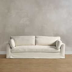 a white couch sitting on top of a hard wood floor next to a gray wall