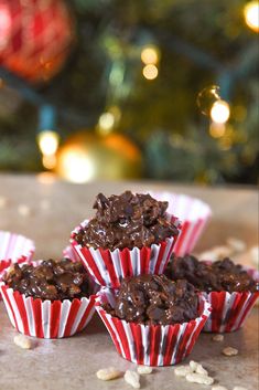 three red and white striped paper cups filled with brownie bites next to a christmas tree