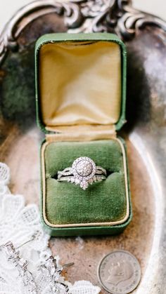 an engagement ring sits in a velvet box on a lace doily next to a quarter penny