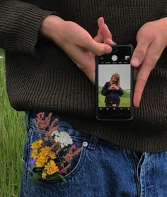 a person taking a selfie with their cell phone in front of some flowers and grass