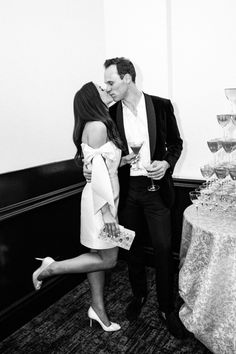 a man and woman standing next to each other in front of a table with wine glasses on it