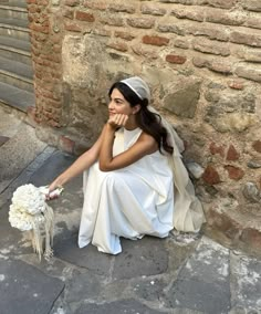 a woman sitting on the ground next to a brick wall holding a bouquet of flowers