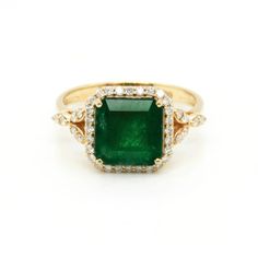 an emerald and diamond ring in yellow gold with diamonds around the band, on a white background