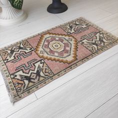 a pink rug on the floor next to a vase with flowers and plants in it