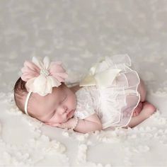 a baby is laying down wearing a white dress and a flower in her hair,