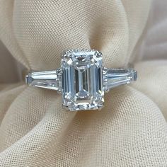 an emerald and baguette cut diamond ring on a white cloth with two bagsuettes