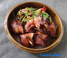 a wooden bowl filled with meat and garnished with green sprigs on top