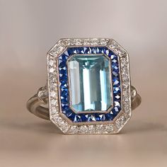 This geometric style platinum ring centers a 2.50 carat natural aquamarine with a lively teal color. Surrounding the center gem is a halo of calibre french cut sapphires followed by a halo of round brilliant cut diamonds. ✦ DIAMOND SPECIFICATIONS: Diamond Cut: Emerald Cut ✦ ENGAGEMENT RING SPECIFICATIONS: Ring Material: Platinum Stones: Aquamarine, Diamond, Sapphire ✦ WHAT COMES IN YOUR SHIPMENT: - Your Engagement Ring - Quality Ring Box - Jewelry Cleaner - UGL Certificate ✦ WHY SHOP WITH US: - Engagement Ring On Hand, Diamond And Sapphire Ring, French Cut, Emerald Engagement Ring Cut, Engagement Rings Platinum