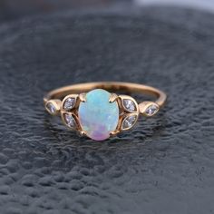 an opal and diamond ring sits on top of a black surface with white stones