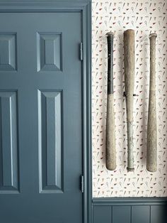 three baseball bats hanging on the wall in front of a blue door with white and red wallpaper