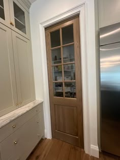 an empty kitchen with white cabinets and wood flooring, along with a stainless steel refrigerator freezer