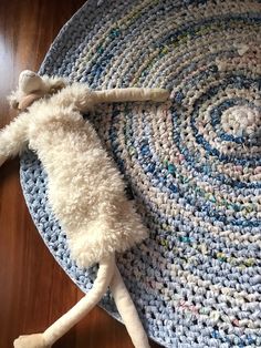 a white stuffed animal laying on top of a blue crocheted rug next to a wooden floor