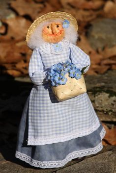 a small doll is dressed in blue and holding a basket with flowers on the ground