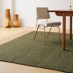 a chair sitting on top of a green rug next to a table and vases