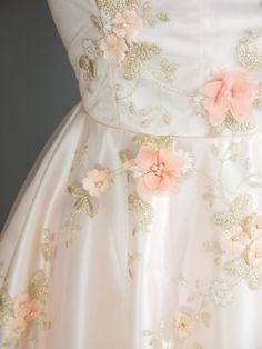 a white dress with pink flowers on the waist and shoulder, is shown in close up