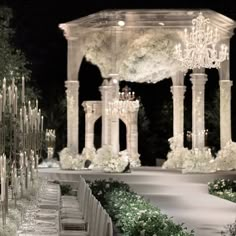 an outdoor wedding setup with white flowers and chandeliers in the background at night