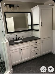 a bathroom with white cabinets and black counter tops is shown in this image, there are two mirrors above the sink