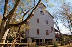 an old house with a water wheel in front of it and trees around the yard